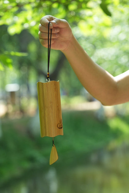 Hand holding a bamboo windchime with a blurred green background