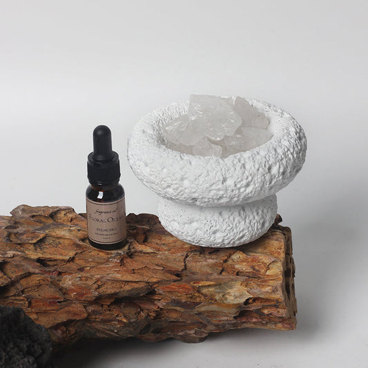 Bottle of essential oil and crystal bowl on a wooden surface with a white background